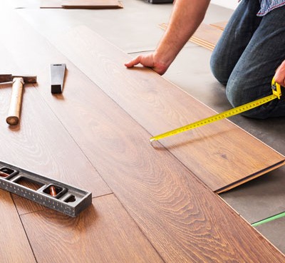 contractor on his knees installing hardwood floor while using measuring tape