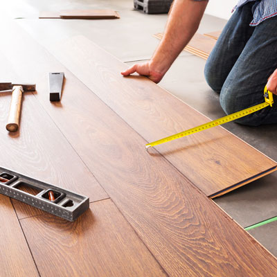 contractor on his knees installing hardwood floor while using measuring tape